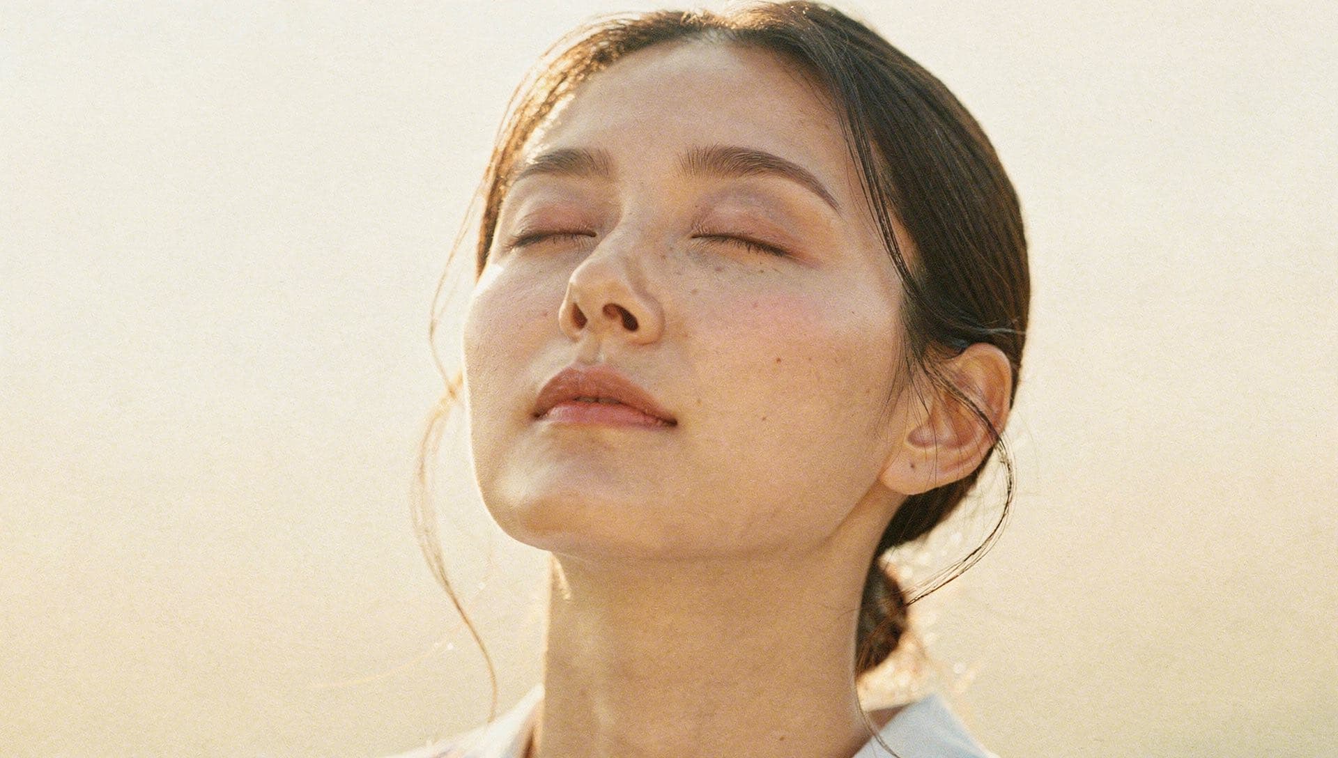 A woman with closed eyes, bathed in warm light against the dark