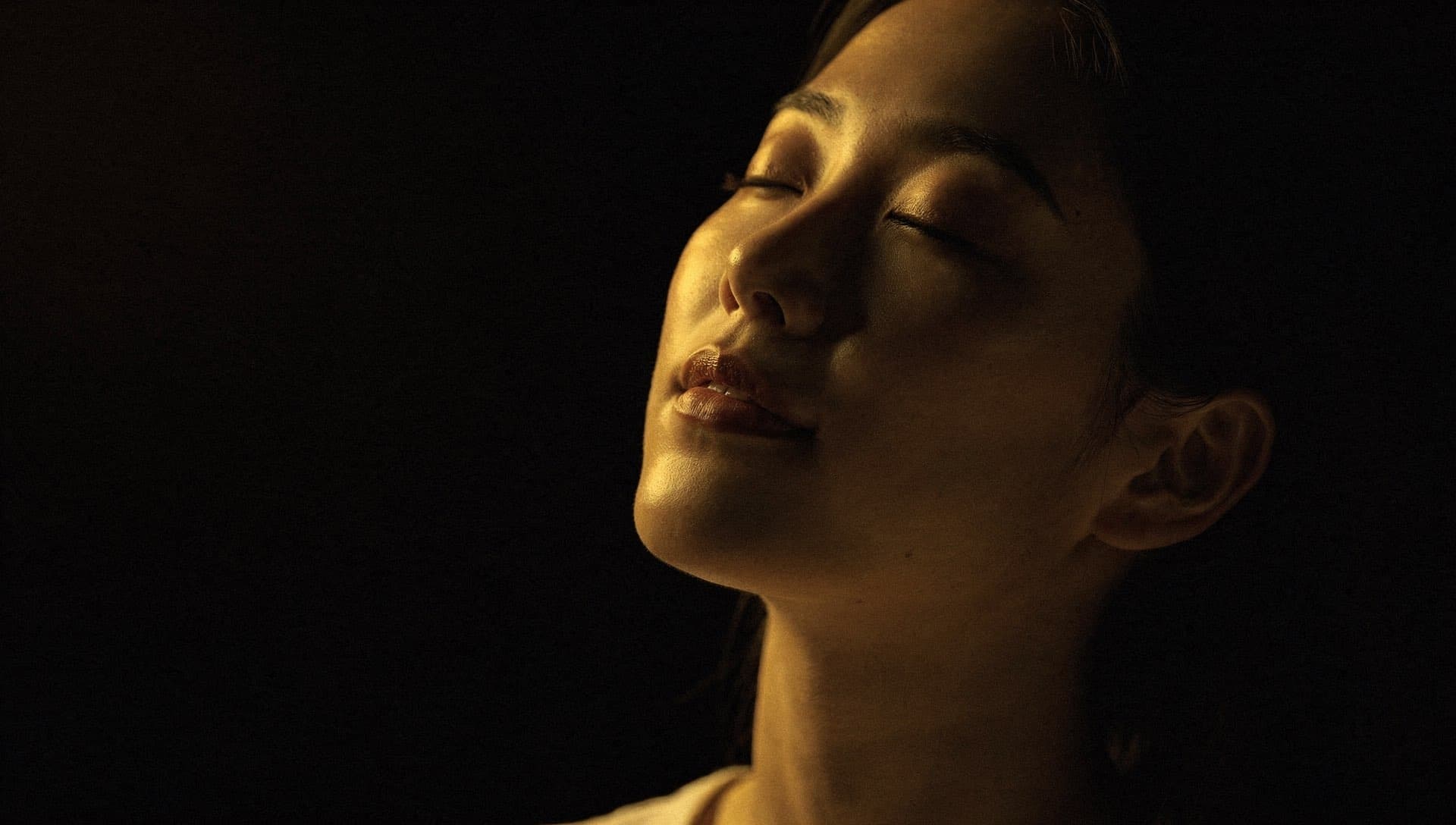 A woman with closed eyes, bathed in warm light against the dark